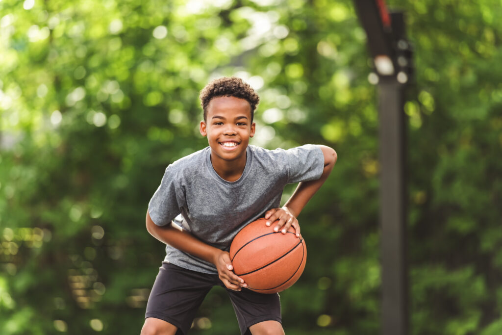 portrait of a boy kid playing with a basketball in park